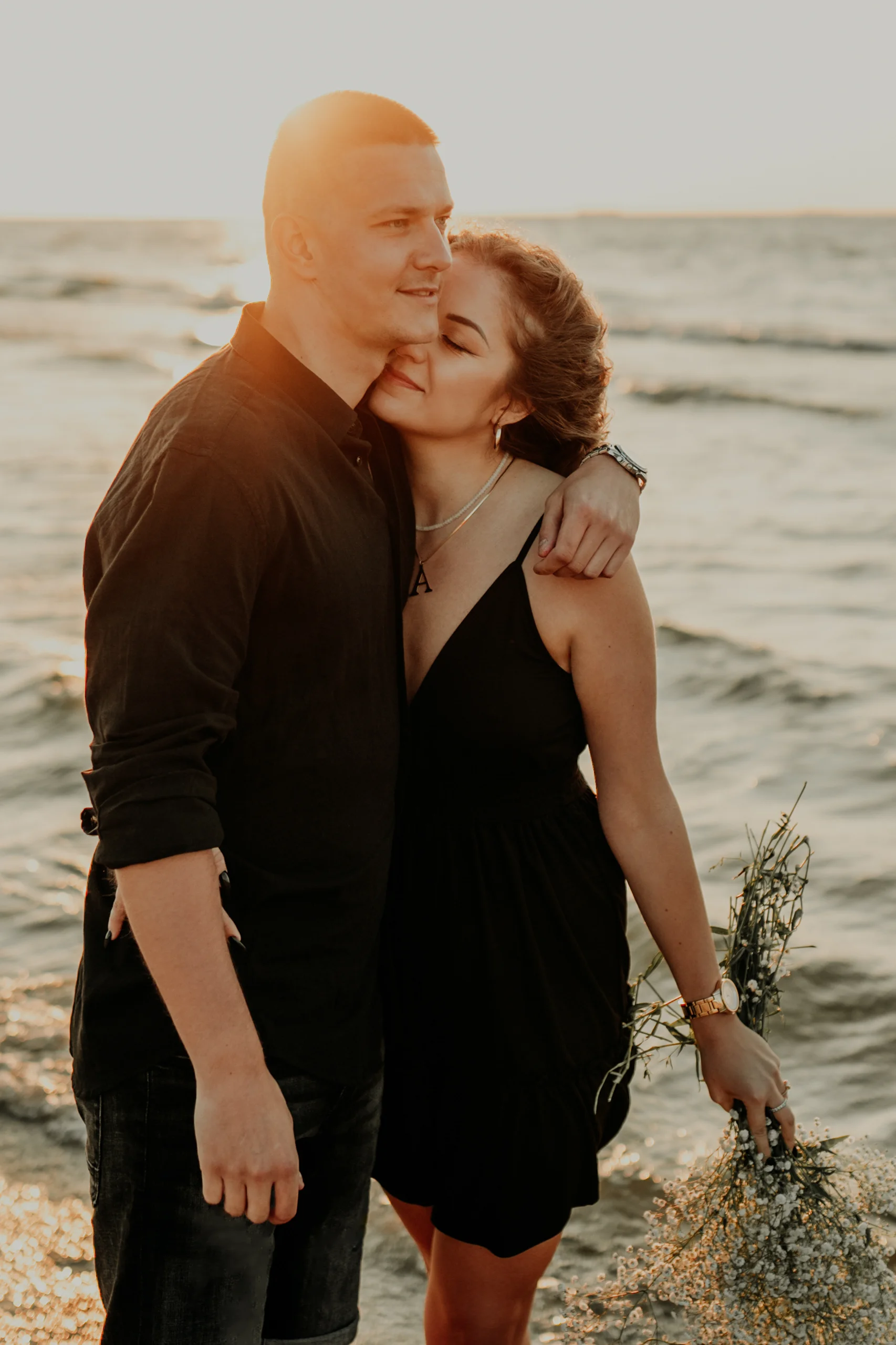 Zakochana para w czarnych strojach przytulająca się na plaży o zachodzie słońca